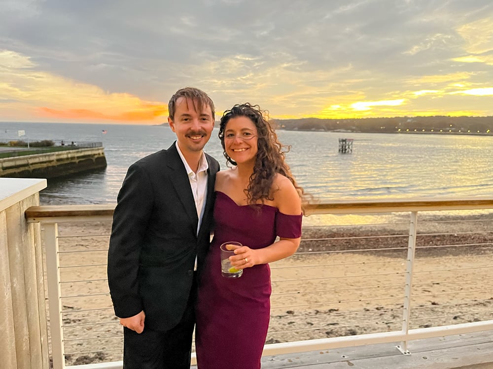 jason with wife erica in front of a sunset by the ocean