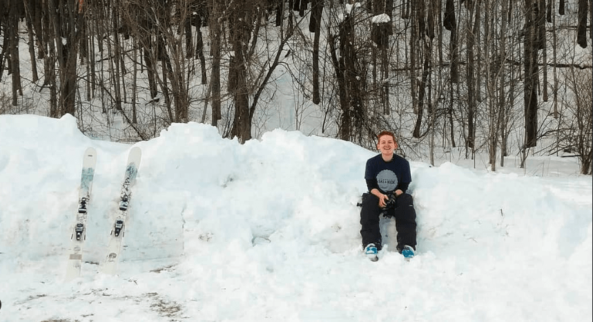 Scott sitting on a pile of snow next to his skis