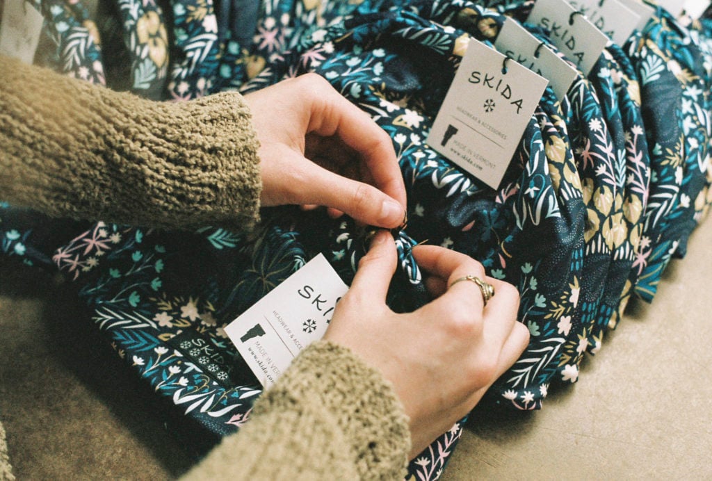 Hands pinning a tag on a Skida hat