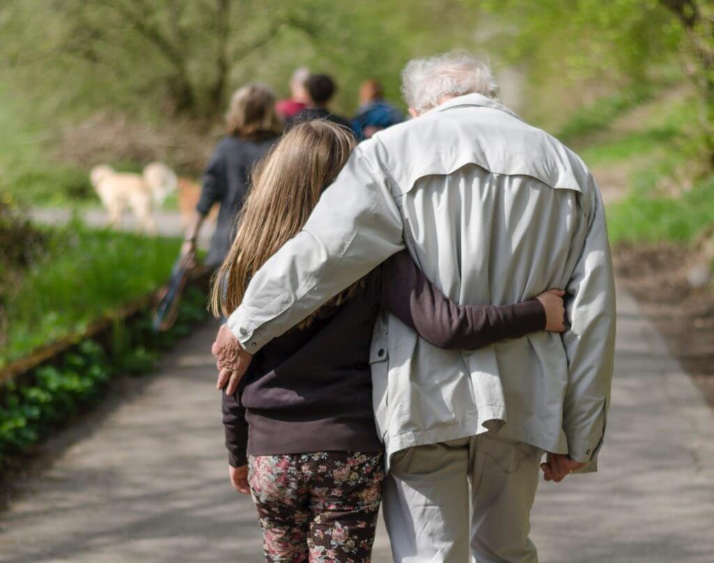 older man and a younger women walking with their arms around eachother