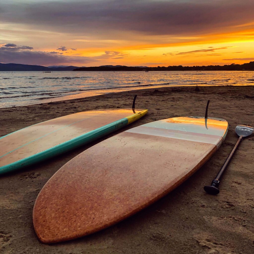 Two stand-up paddleboards by a beach at sunset
