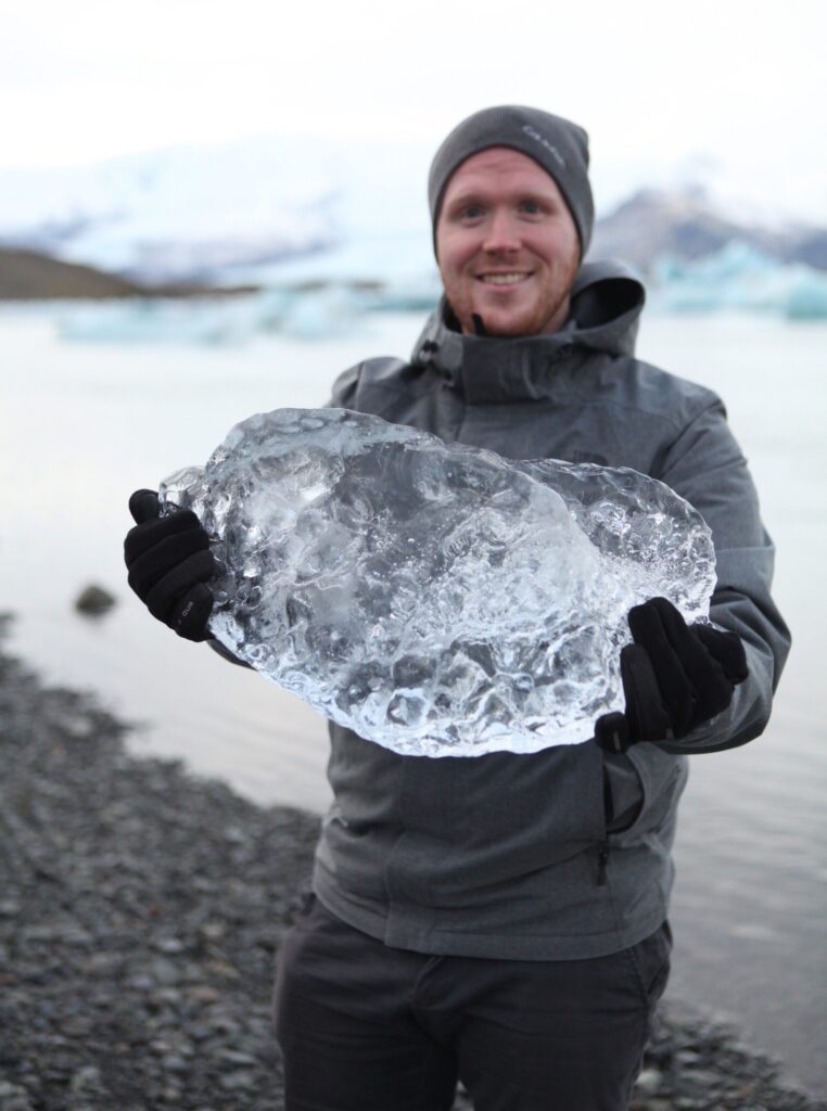 Josh holding a large block of ice in front of a body of water