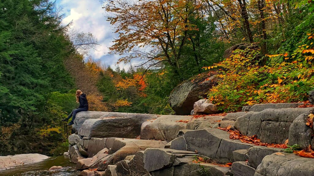 Emily sitting on a large rock face among a fall foliage scene