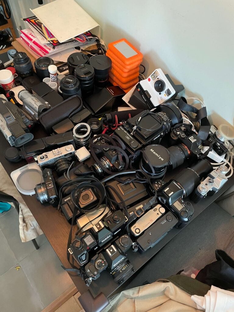 a table with lots of cameras, lenses, hard drives and camera accessories