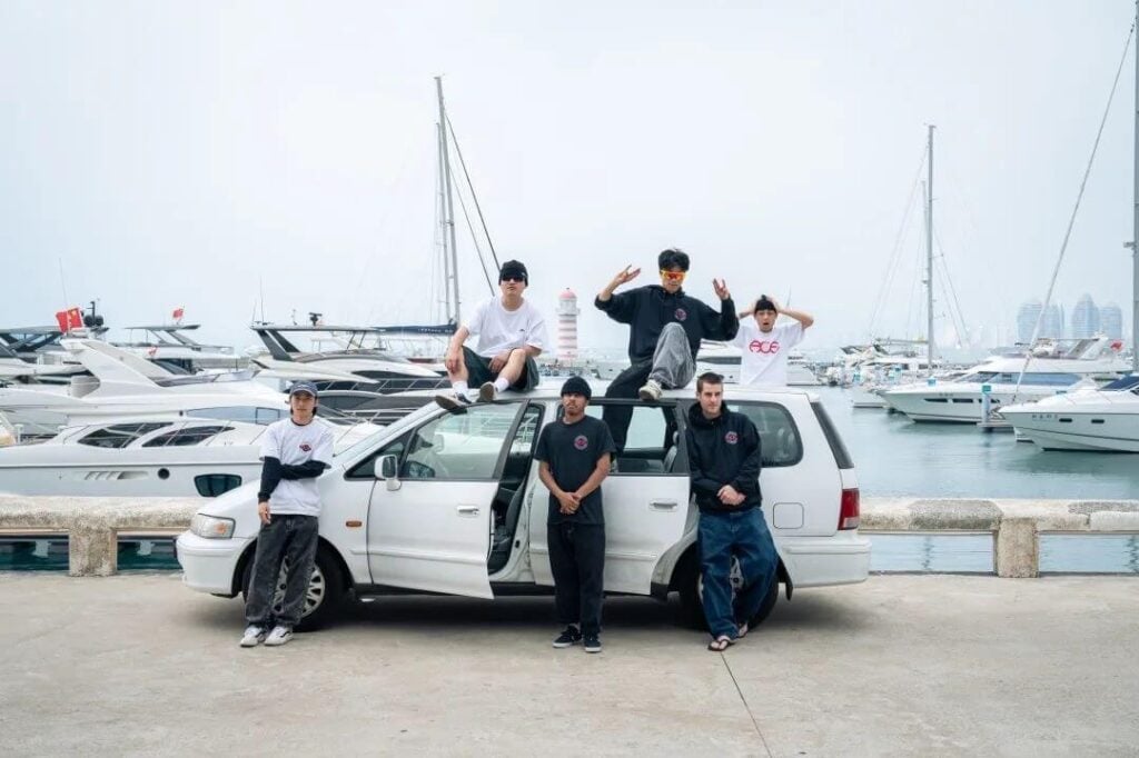 a group of 6 men around an old white Chrysler mini van parked next to a marina