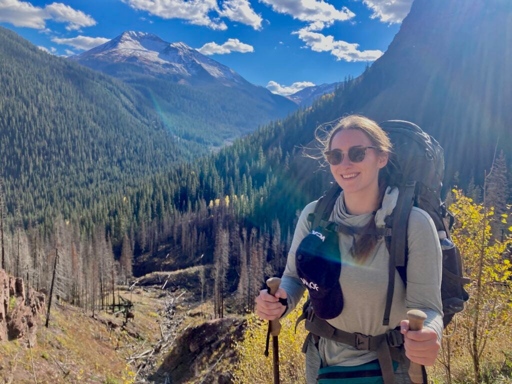 Cat with a backpack and trekking poles, smiling in front of a Colorado mountain view