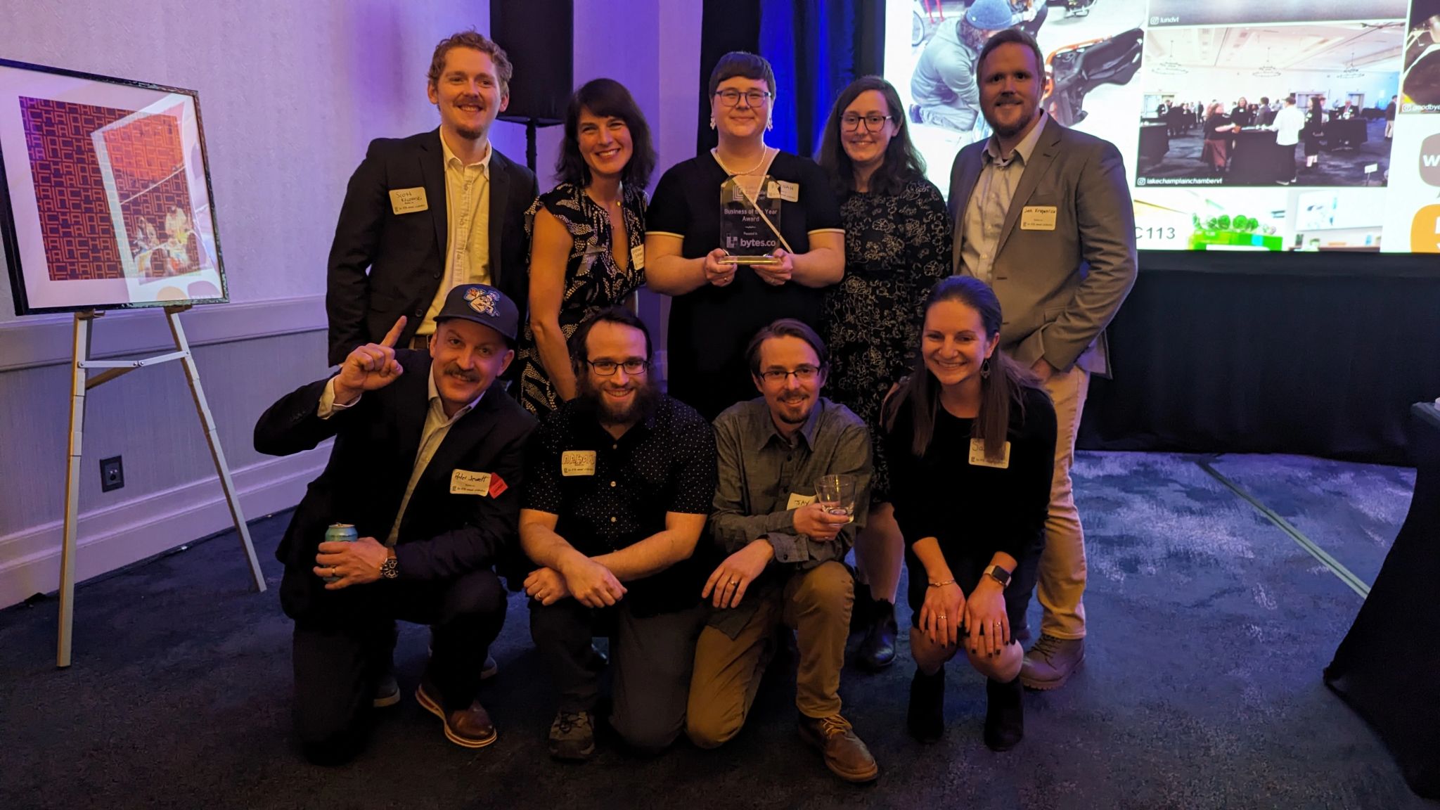 The Bytes.co team standing and kneeling together for a group photo after accepting the Lake Champlain Chamber 2024 Business of the Year award. From left to right: Scott Kliczewski, Kristina Drobny, Hannah Hook, Lilly Romano, Josh Kirkpatrick, Peter Jewett, Aaron Silber, Jay Di Vece, and Sarah Maines.