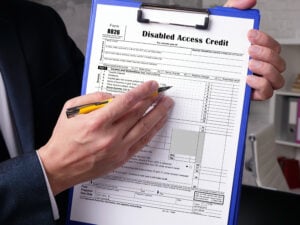 A man holding a pencil and a clipboard with Form 8826 of the Disabled Access Credit on it