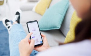 A woman browsing a website for homepage design inspiration on her iPhone while sitting on her couch