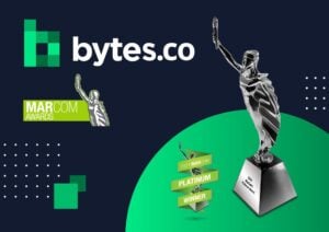 The Bytes.co and MarCom Awards logos together next to the Silver 2024 MarCom Awards winner logo and trophy statuette on a navy blue and green background