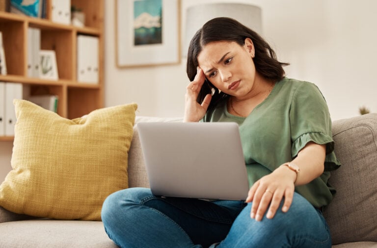 A frustrated woman sitting on a couch and running into user friction barriers while browsing a site on her laptop