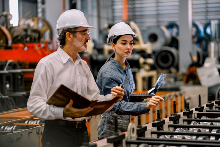 A man and a woman in hardhats discussing operations in a factory