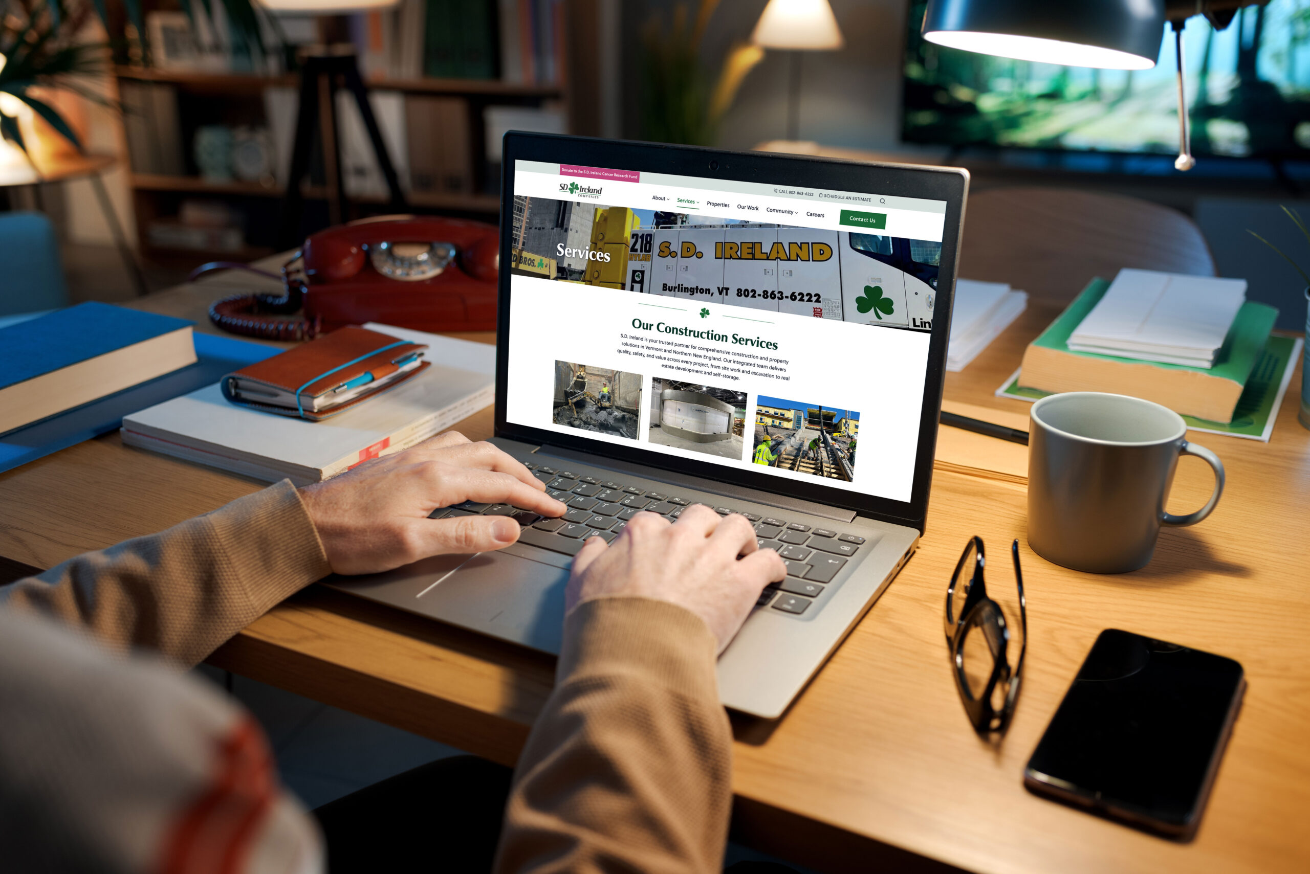 A man sitting at his desk looking at the S.D. Ireland Construction Services page on a laptop