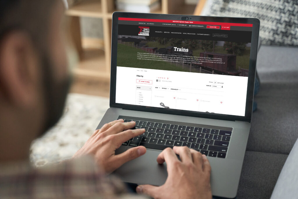 A man sitting on the couch while browsing the Tony's Train Exchange Model Trains page on his laptop